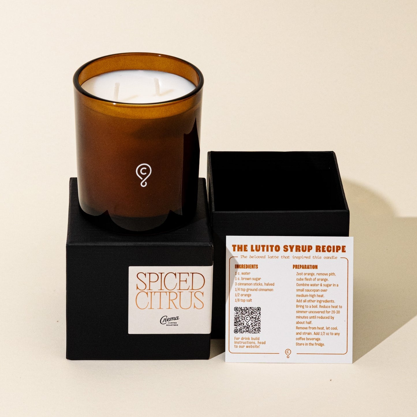 A Spiced Citrus scented candle with a white wax blend, poured into an amber glass vessel, displayed next to its black box packaging with information card.